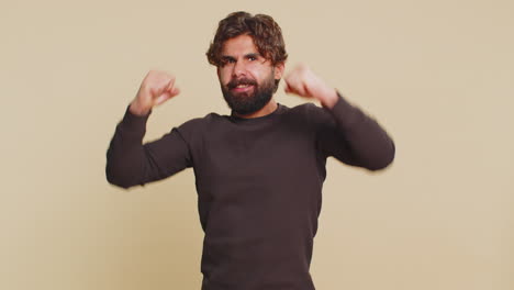 feliz joven indio dedos cruzados gritando celebrando el éxito contra un fondo beige