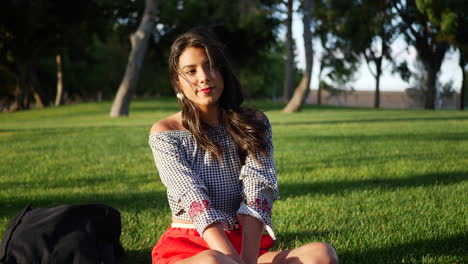 beautiful young hispanic college student resting on a grassy park field on a calming sunny day