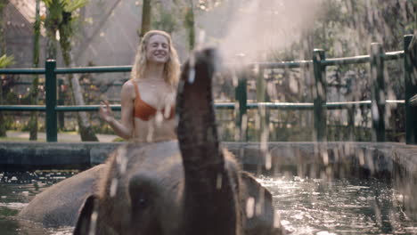 Hermosa-Mujer-Montando-Elefante-En-El-Zoológico-Jugando-En-La-Piscina-Rociando-Agua-Turista-Divirtiéndose-En-Vacaciones-Exóticas-En-El-Santuario-Del-Bosque-Tropical