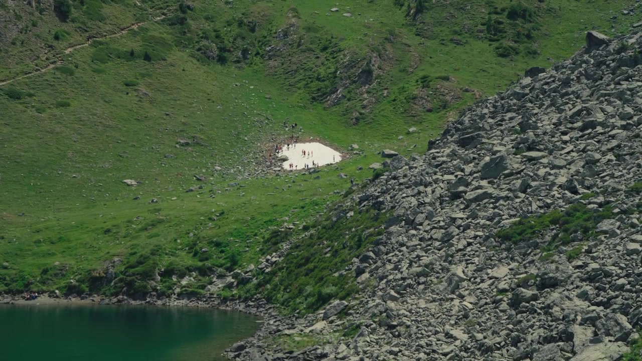 Gruppo di persone che si godono un sentiero di montagna innevato accanto a un lago alpino e un prato, circondati da cime spettacolari, che cattura l'amicizia, l'avventura all'aria aperta e la ricreazione invernale