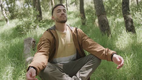 African-american-man-sitting-on-tree-trunk-and-meditating-in-forest,-slow-motion