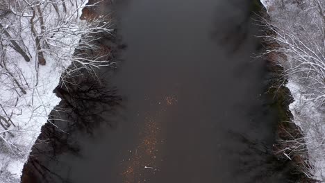Drone-shot-of-a-shallow-slow-moving-river-during-winter-time-with-snow-covering-the-land