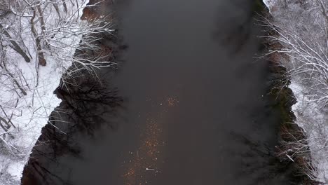 toma de un dron de un río lento y poco profundo durante el invierno con nieve cubriendo la tierra