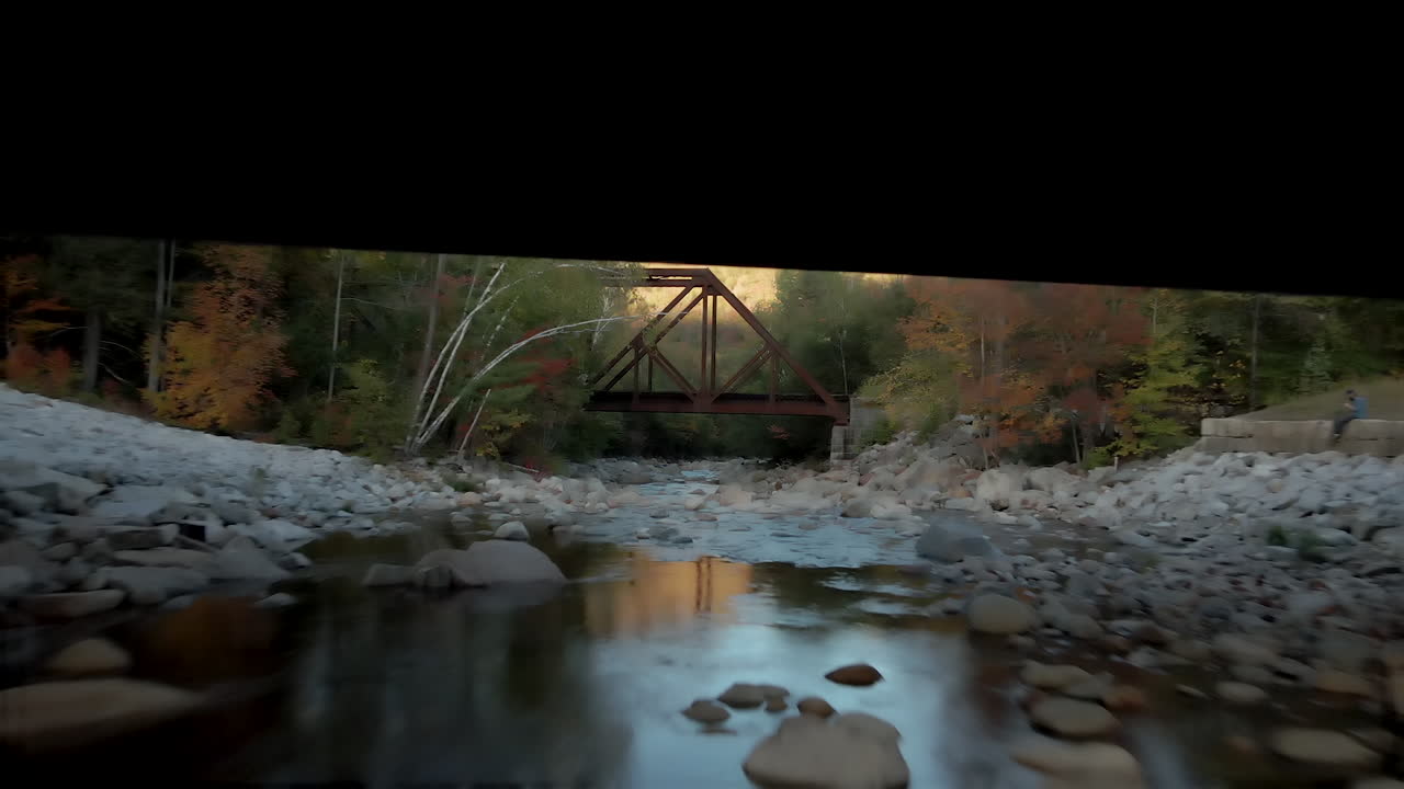 Long shot from still river surface under bridge over old bridge revealing mountains and foliage
