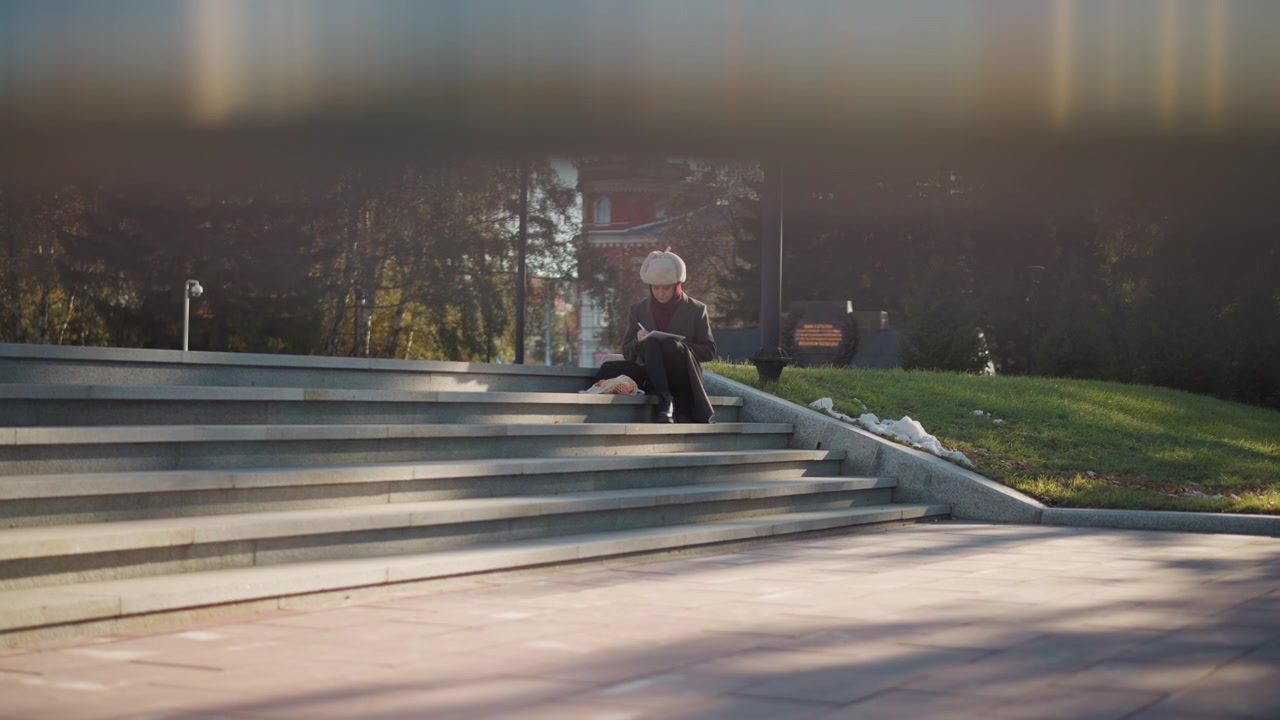 Young Woman Sitting on Park Steps Writing in Notebook