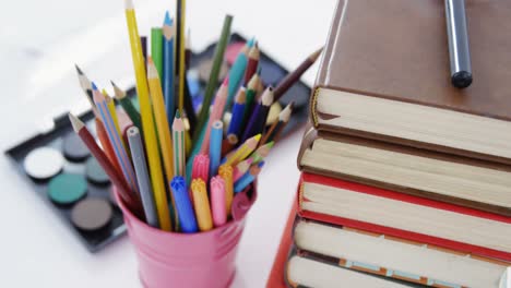 colored pencils in pen holder with pile of books