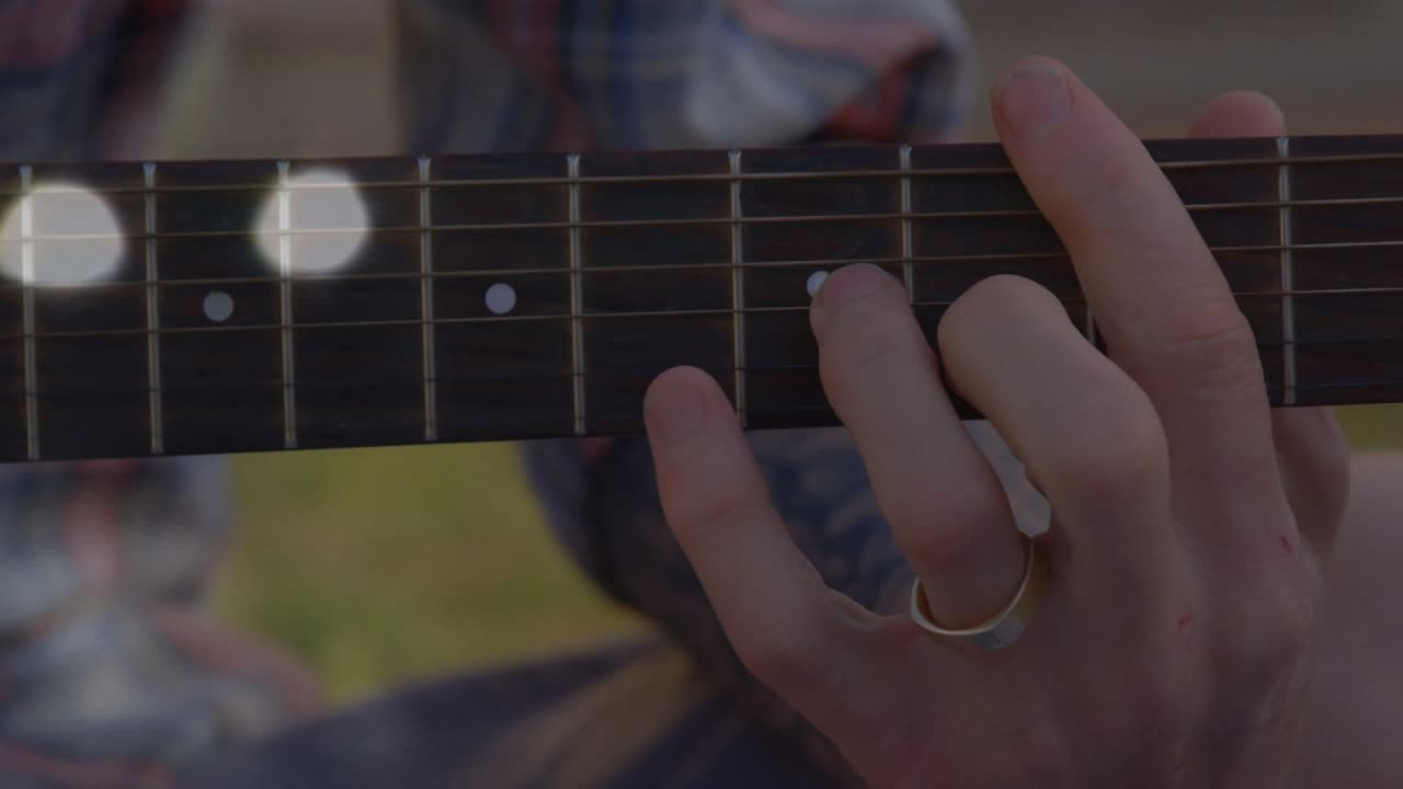 Gitarrist som glider med fingrarna på halsen efter musiksignalen, bokeh-reflexer som driver över banden och ändrar ackord