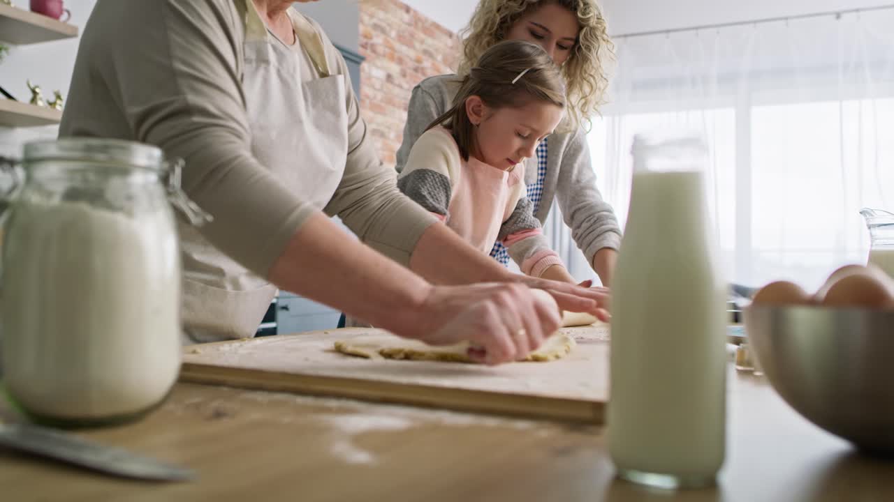 Tilt up video of three generations of women rolling dough