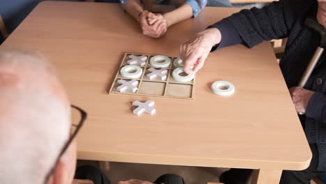 senior friends playing tic tac toe at table in nursing home