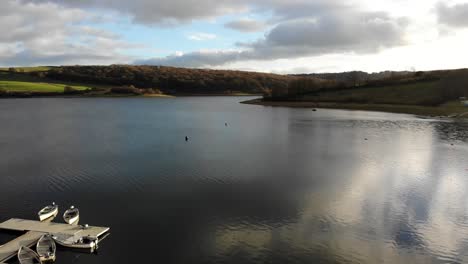 Aerial-backwards-shot-of-Wimbleball-Lake-Exmoor-UK-to-reveal-moored-boats-at-the-side-of-the-Lake