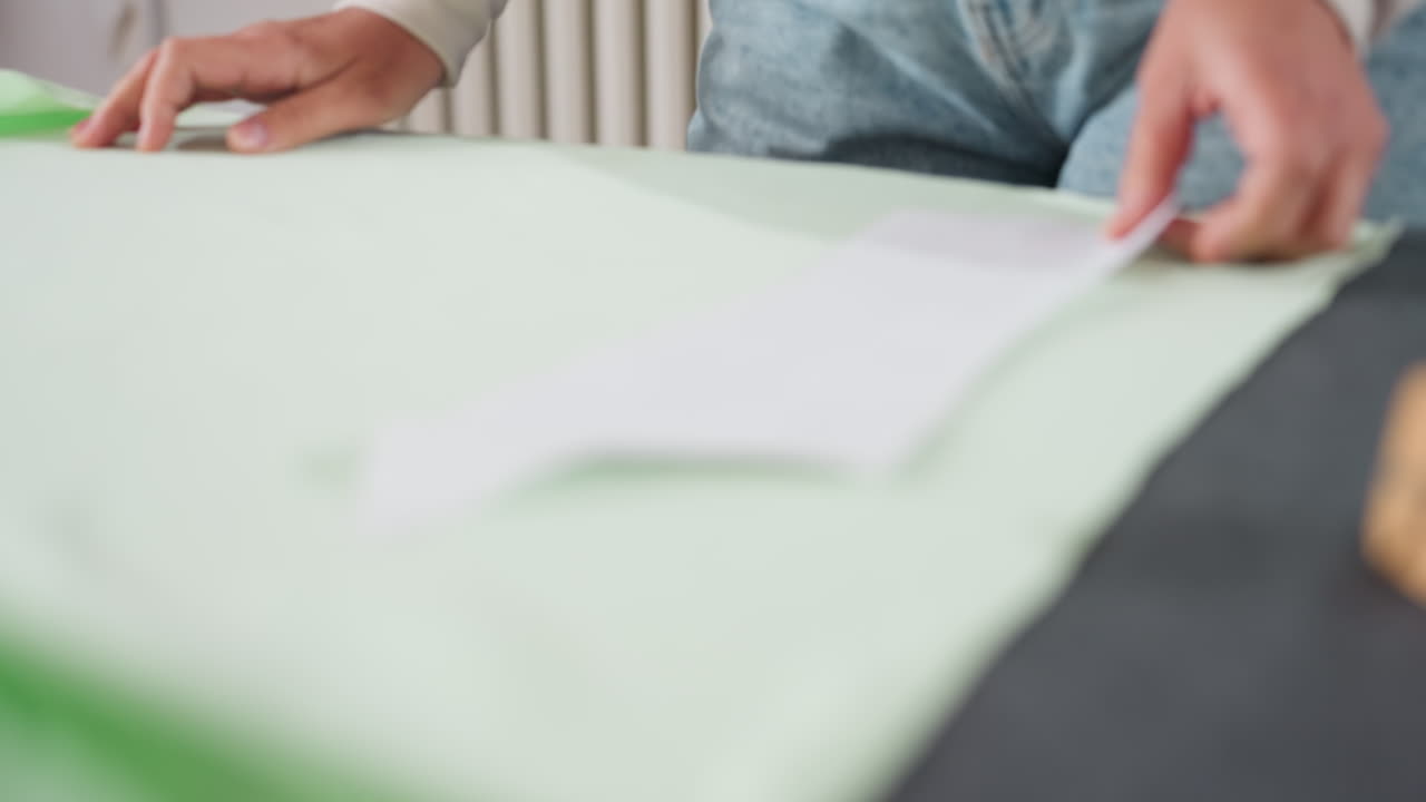 Female tailor carefully places cut out paper design over light green elastic fabric on workspace table in sewing studio, preparing material layout for precise cutting and creative garment making