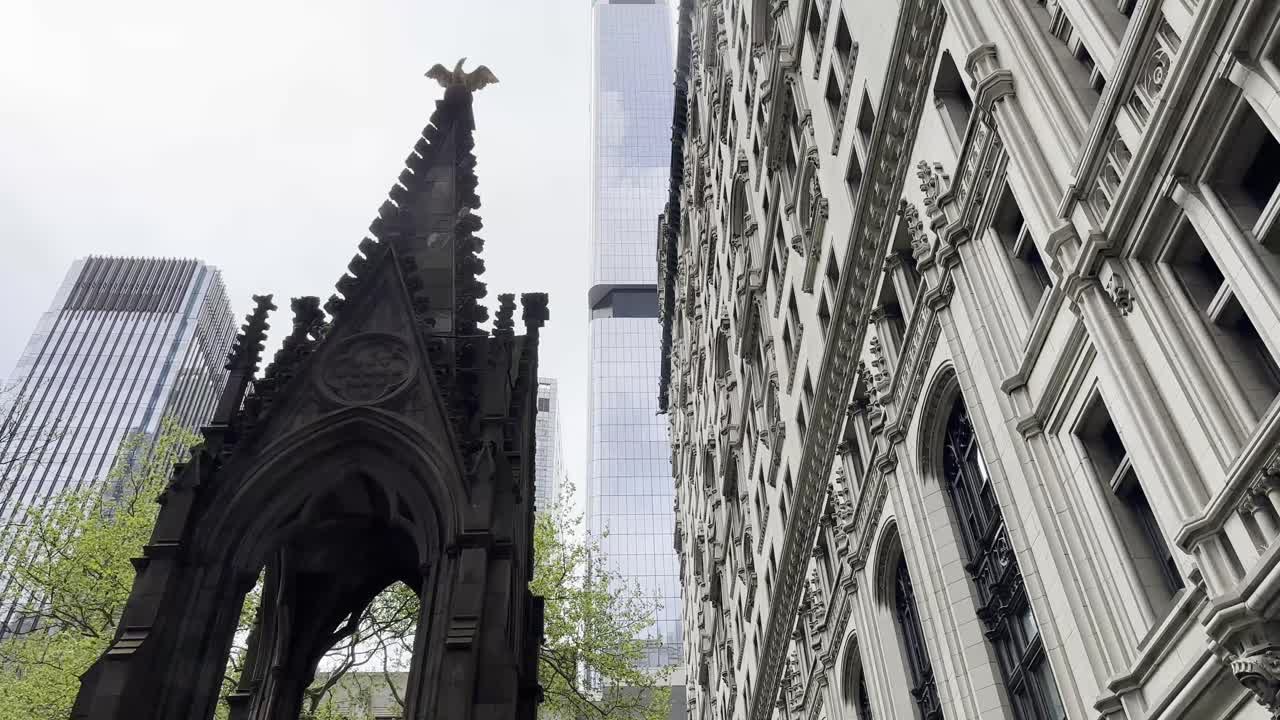 트리니티 교회 (trinity church) 의 복잡한 고 건축물이 맨해튼 하부 (lower manhattan) 의 현대적인 마천루와 맞아있는 클로즈업 뷰 (close-up view) 는 도시의 역사적이고 현대적인 디자인의 혼합을 강조합니다.