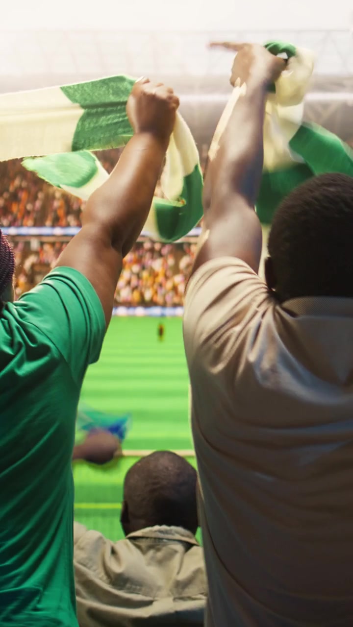 Video vertical: Primer plano de aficionados al fútbol celebrando dentro de un estadio lleno.