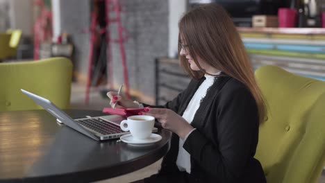 mujer de negocios tomando café mientras toma notas frente a una laptop en una cafetería