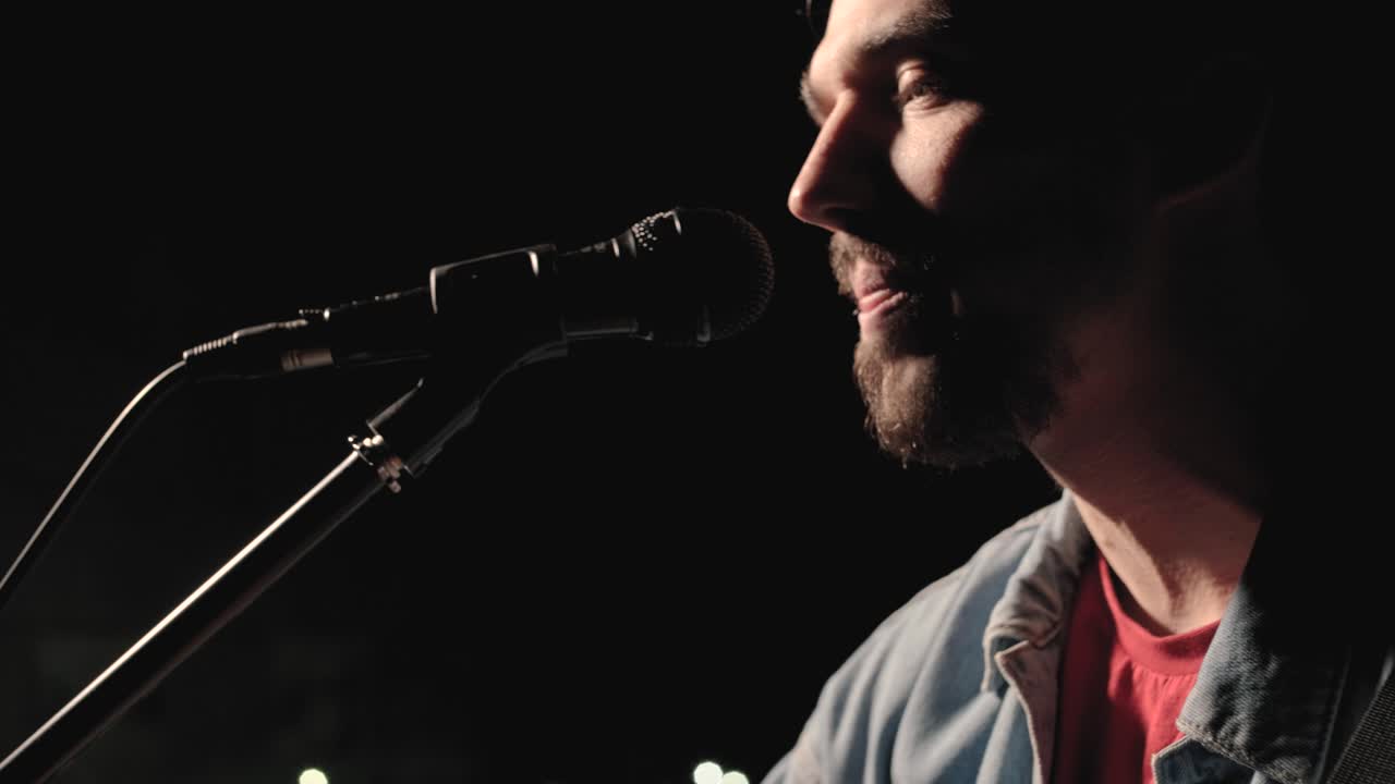 un músico está tocando la guitarra en un gran escenario con miembros de la audiencia sosteniendo linternas en el fondo. el auditorio está lleno de hermosas luces parpadeantes.