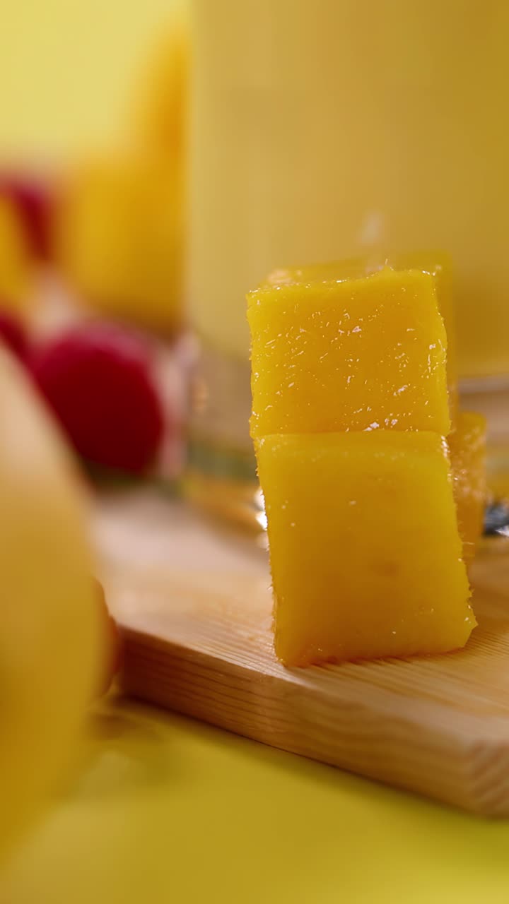 Primo piano di cubetti di mango, frullato, lamponi e banana su sfondo giallo brillante, messa a fuoco superficiale