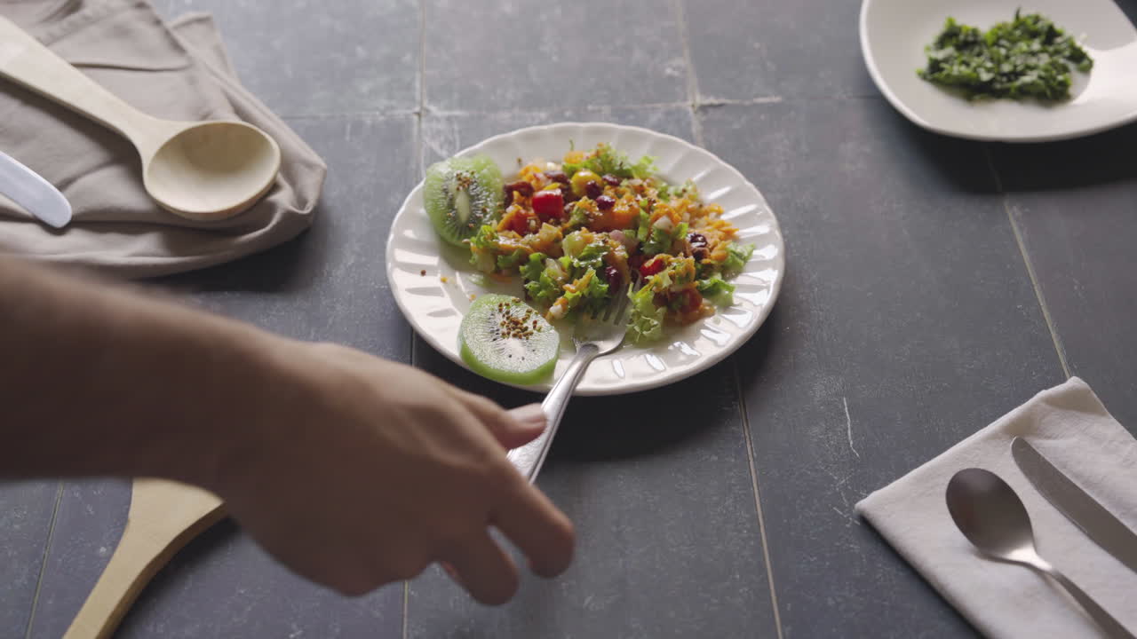 la mano del hombre pone una horquilla en el plato con ensalada de frutas y verduras