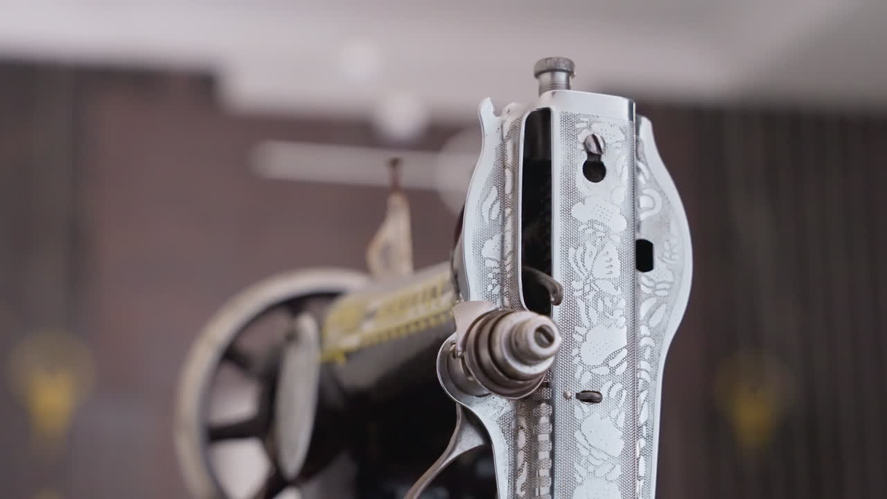 Close-up de máquina de costura preta em oficina caseira, com corpo de metal vintage e roda manual, enquanto a costureira guia o tecido sob a agulha. Foco na linha, bobina, sapatilha e formação do ponto. Clima acolhedor e nostálgico.