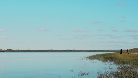 Scene-of-a-calm-lake-with-two-people-standing-on-the-shore-and-fishing