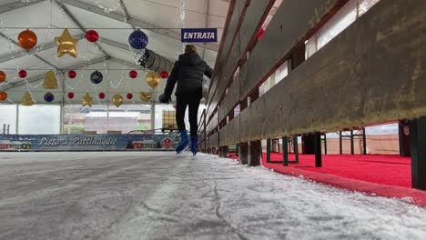 Little-girl-skating-on-ice-alone-in-empty-indoor-ice-rink-with-Christmas-decorations