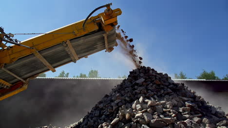 a conveyer dumps rocks that have been pulverized by a crusher on a pile at an aggregate quarry in slow motion