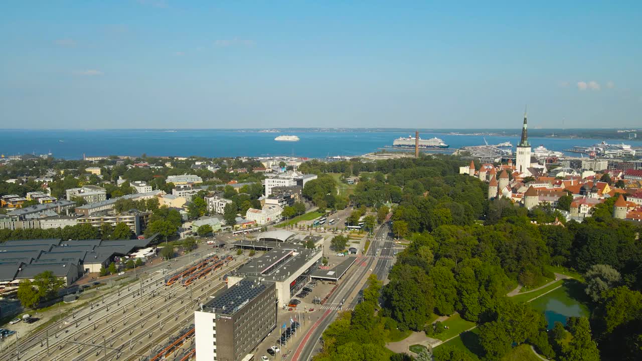 Aerial drone footage video of Tallinn city modern railroad or train station and historic medieval old city walls with church towers and limestone buildings during a sunny summer day, ocean visible
