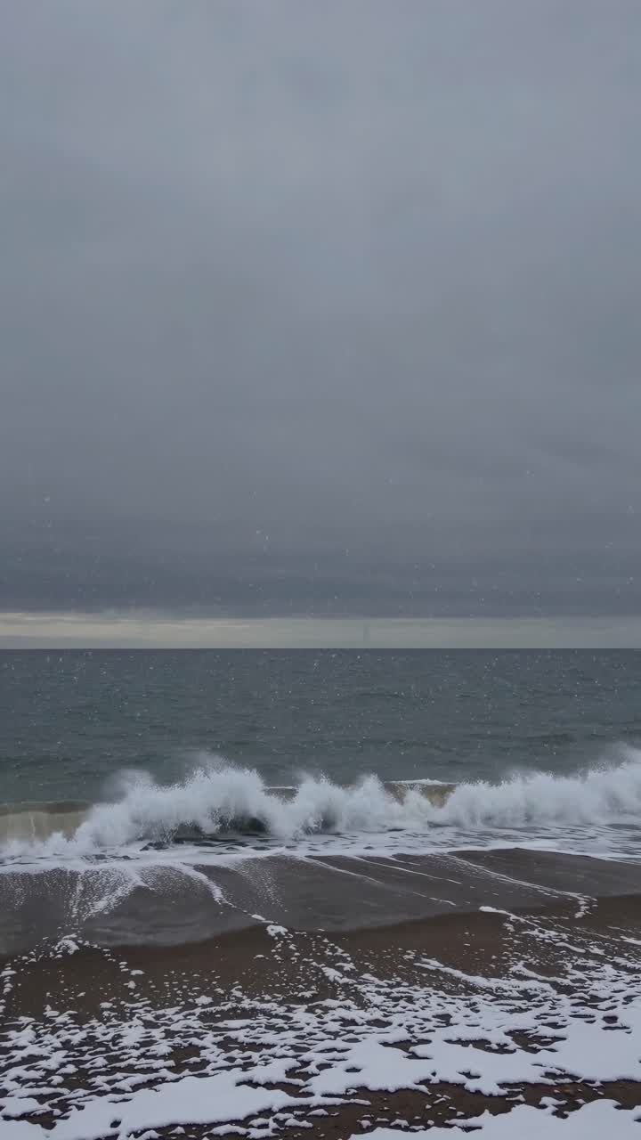 A serene video of waves crashing on a snowy beach, captured from a low-angle