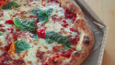 closeup shot of tasty neapolitan pizza with pesto sauce in a cardboard pizza box on the table, rotating shot