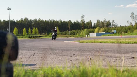 biker on motorbike riding turn on forest race track, then wave by hand