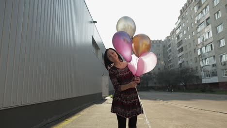 Pretty-woman-in-dress-holding-balloons-with-helium-outdoors-in-daylight