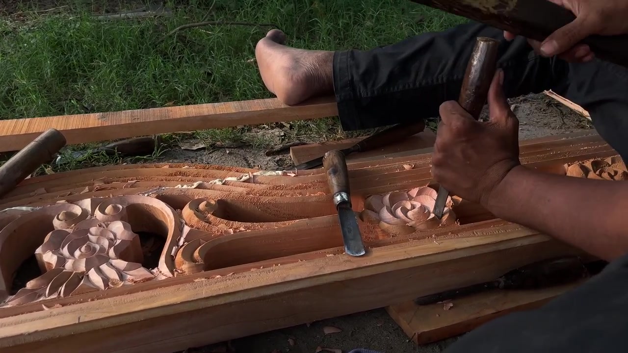Closeup of craftsman carving intricate floral pattern into wooden panel with chisel and mallet, shaping decorative relief by hand during woodworking process.