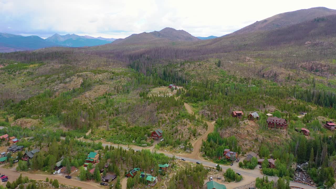Vista aerea di una comunità montana con baite, strade tortuose, ricrescita forestale e pendii alpini scoscesi che si estendono attraverso una spettacolare valle di alta montagna in estate.