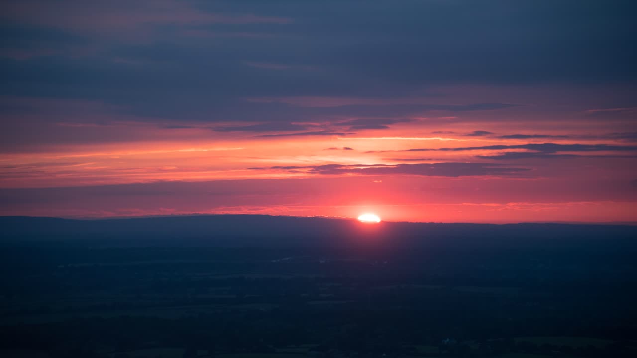 Sun setting through clouds and hill, South Downs, UK