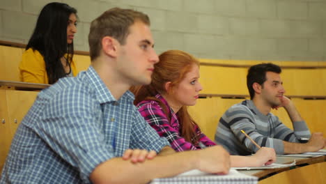 Focused-students-listening-in-lecture-hall-and-taking-notes