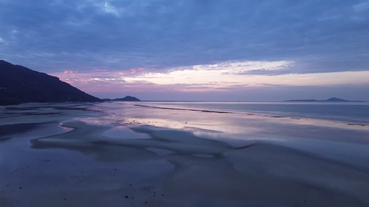 Beautiful aerial drone footage of sunrise over Koh Phangan, Thailand, featuring a pink horizon, calm sea, tropical coastline, and scenic island landscape in morning light