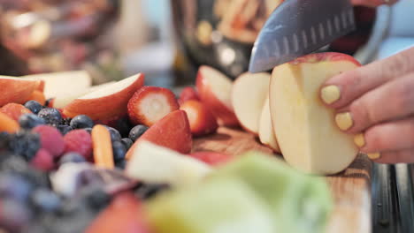 Woman-slicing-apple-on-cutting-board-filled-with-fresh,-colorful-produce