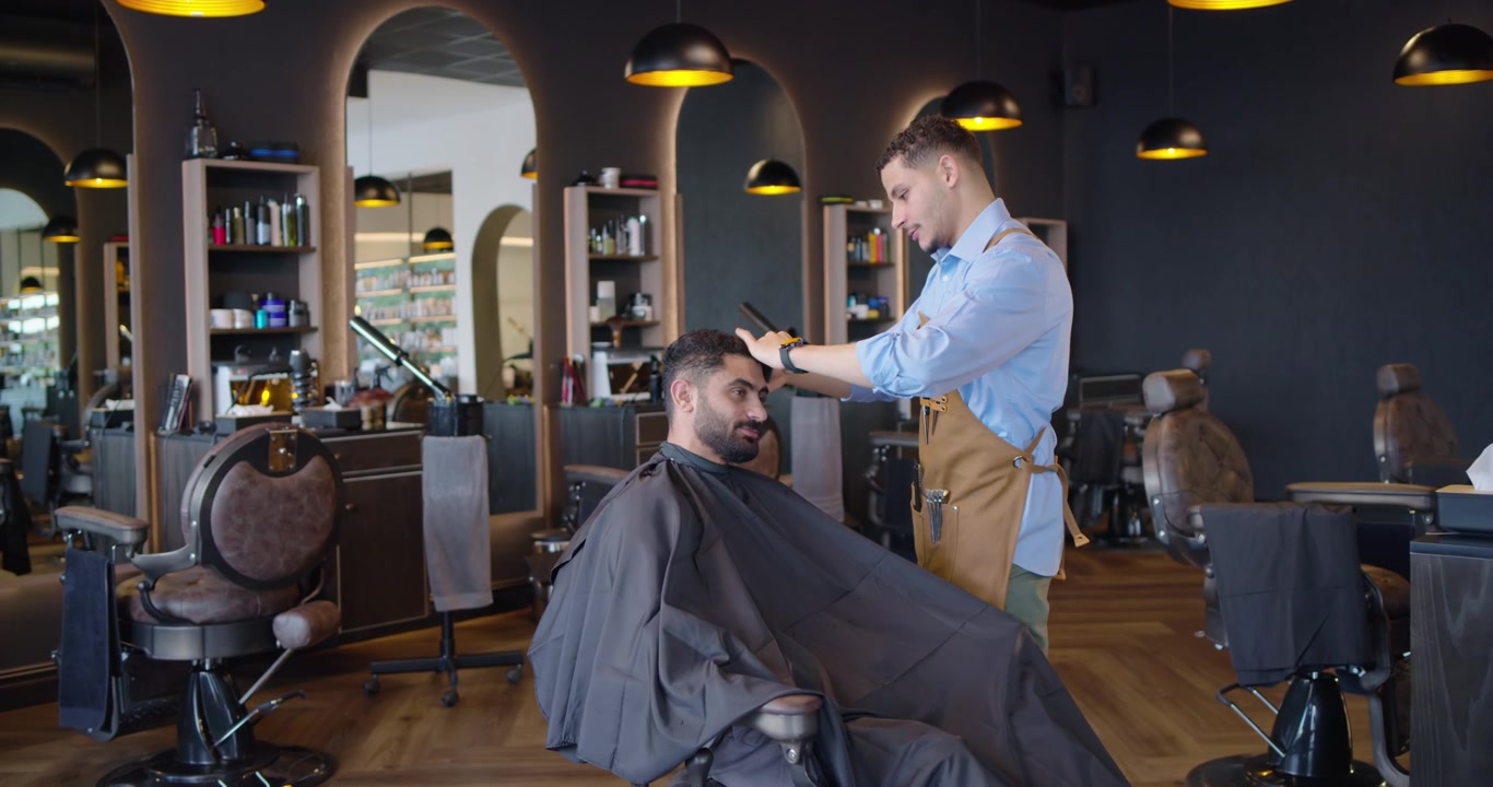 Barbiere africano che taglia i capelli a un cliente uomo reclinato con pettine e forbici in un salone, mentre modella il taglio.