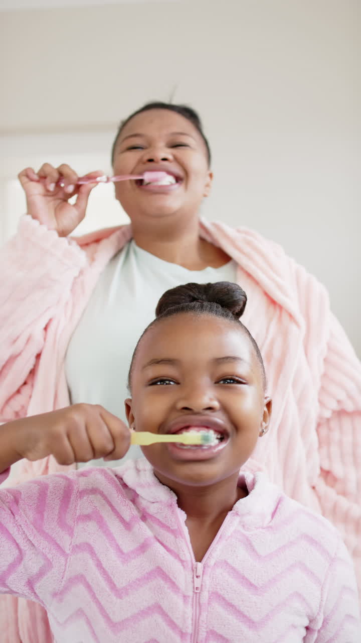 Video verticale di madre e figlia afroamericane felici che si lavano i denti, al rallentatore