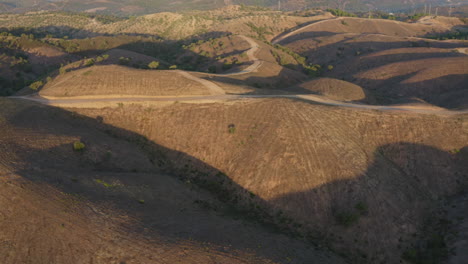 Flyover-Tilt-Down-Shot-of-dirt-roads-on-top-of-barren-and-dry-hills-in-Algarve,-Portugal