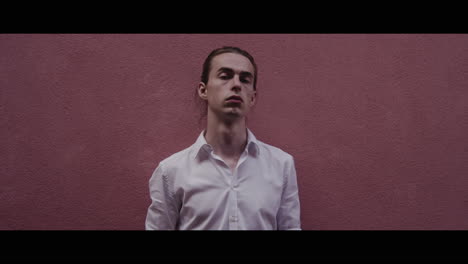 young man in white shirt against a pink wall