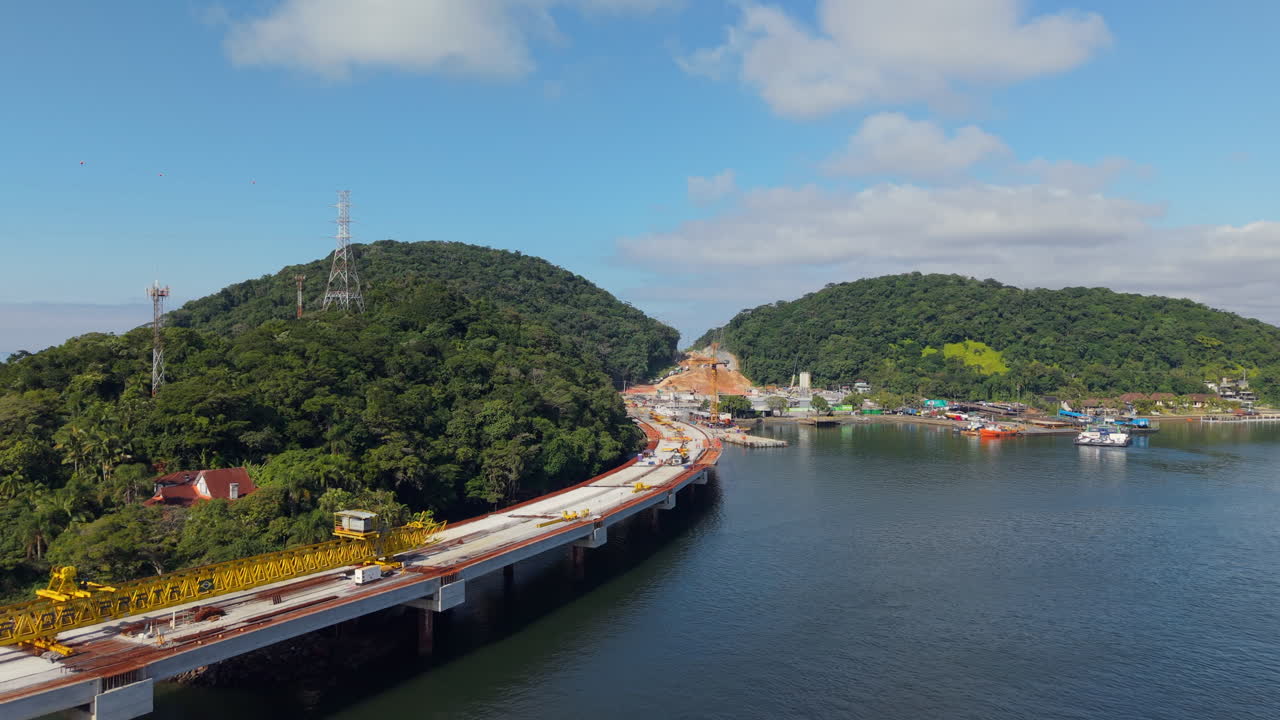 Slow approaching aerial movement to the construction works from the new Guaratuba-Matinhos Bridge with bay coastal port, Paraná, Brazil