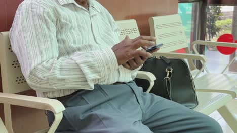 older man sitting and using his phone in a waiting room
