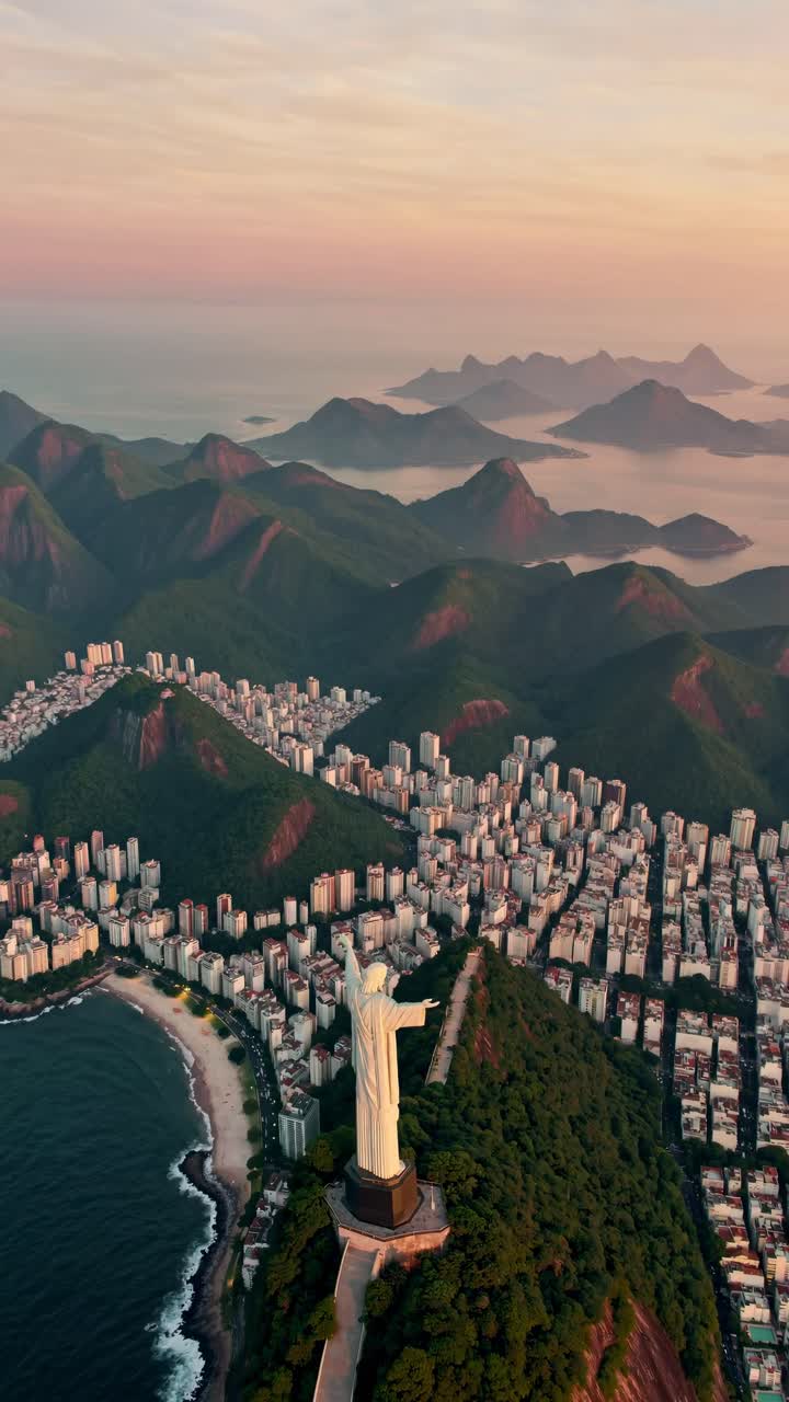 Aerial video view of a cityscape with iconic statue, surrounded by lush mountains and ocean