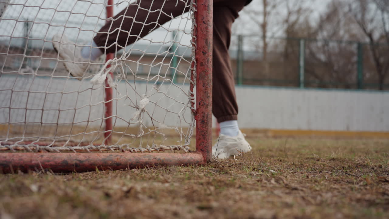 white sneaker at net edge closeup, foot tapping rusty post on dry pitch; subtle net sway, textured ground and casual training steps, quiet practice mood ideal for sports edits and instructional clips