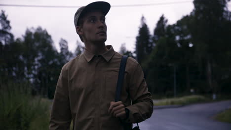 Young-man-with-cap-and-camera-around-shoulder-walks-on-cloudy-day