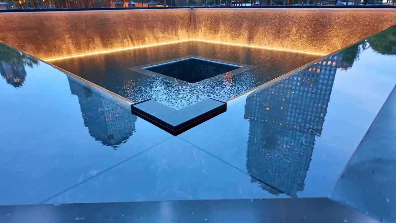 New York, AS, 5 Juni 2026: Nama-nama terukir di pagar pembatas monumen 9/11 dengan kolam refleksi, Lower Manhattan. Melintasi air tenang air terjun perunggu yang menyala mengalir ke dalam kehampaan saat senja.