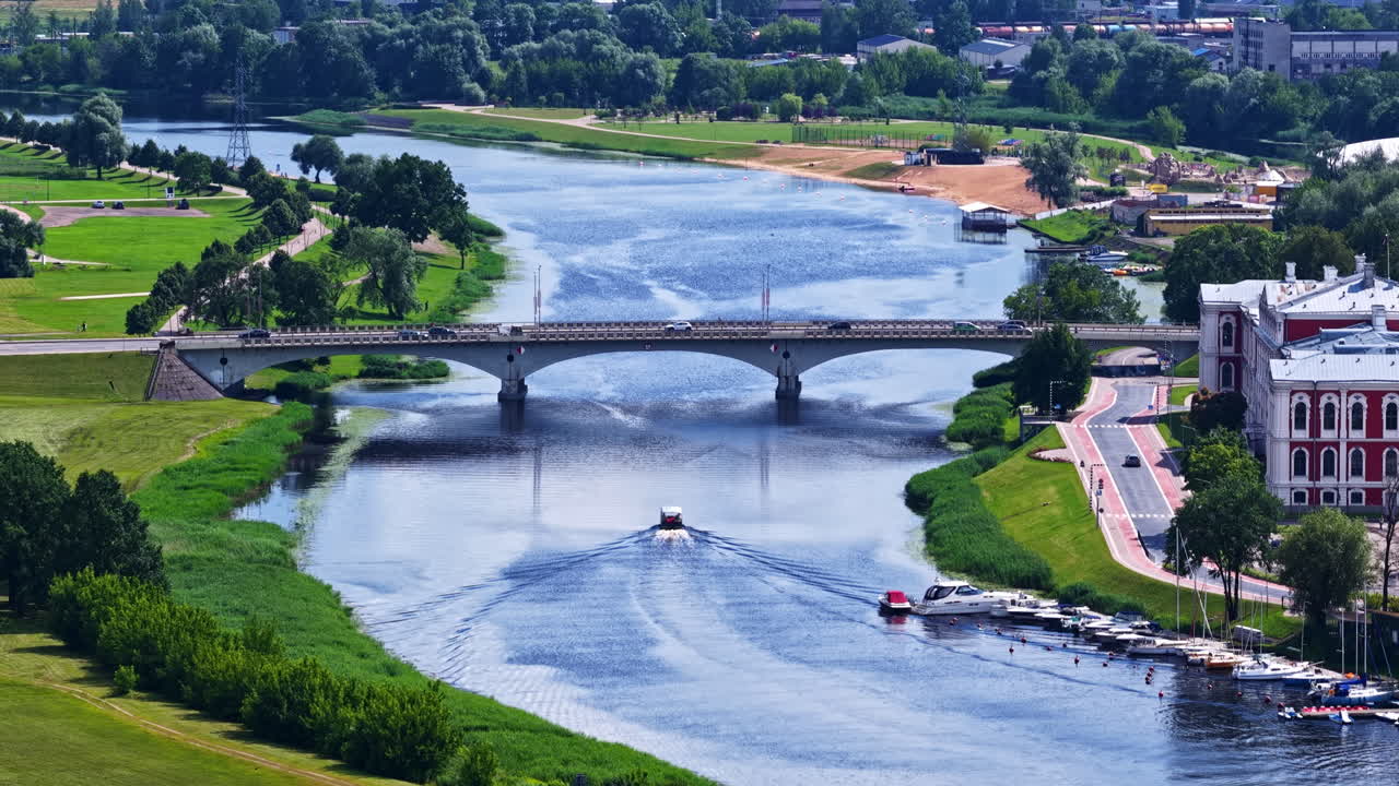 Summer traffic on the Lielupe Bridge and a boat on the river, with the historic Jelgava Palace visible on the riverbank in Jelgava, Latvia - An aerial drone shot
