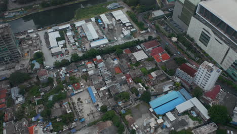 Aerial-tilting-view-into-overhead-shot-of-dense-urban-neighborhood-surrounded-by-tall-skyscrapers-in-Jakarta,-Indonesia