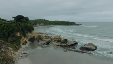 Aerial-view-of-rugged-sandy-bay-with-waves-rolling-in-from-the-Tasman-Sea-at-Omau-Cliffs,-Cape-Foulwind-on-the-West-Coast-of-South-Island,-New-Zealand-Aotearoa