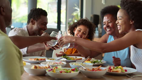 Familia-Multigeneracional-Alrededor-De-La-Mesa-Haciendo-Aplausos-Con-Agua-Antes-De-Servir-Comida-En-Casa